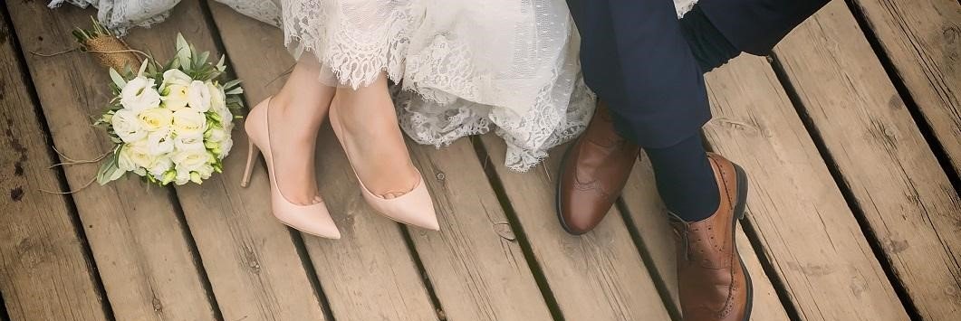 Bride and groom shown from the knees down holding hands while sitting