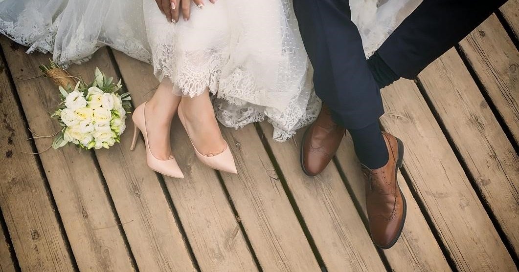 Bride and groom shown from the knees down holding hands while sitting