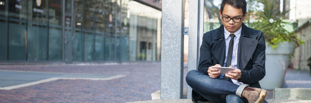 A well-dressed man on sitting on a stone bench and reading something on his phone.