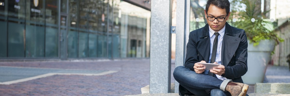 A well-dressed man on sitting on a stone bench and reading something on his phone.