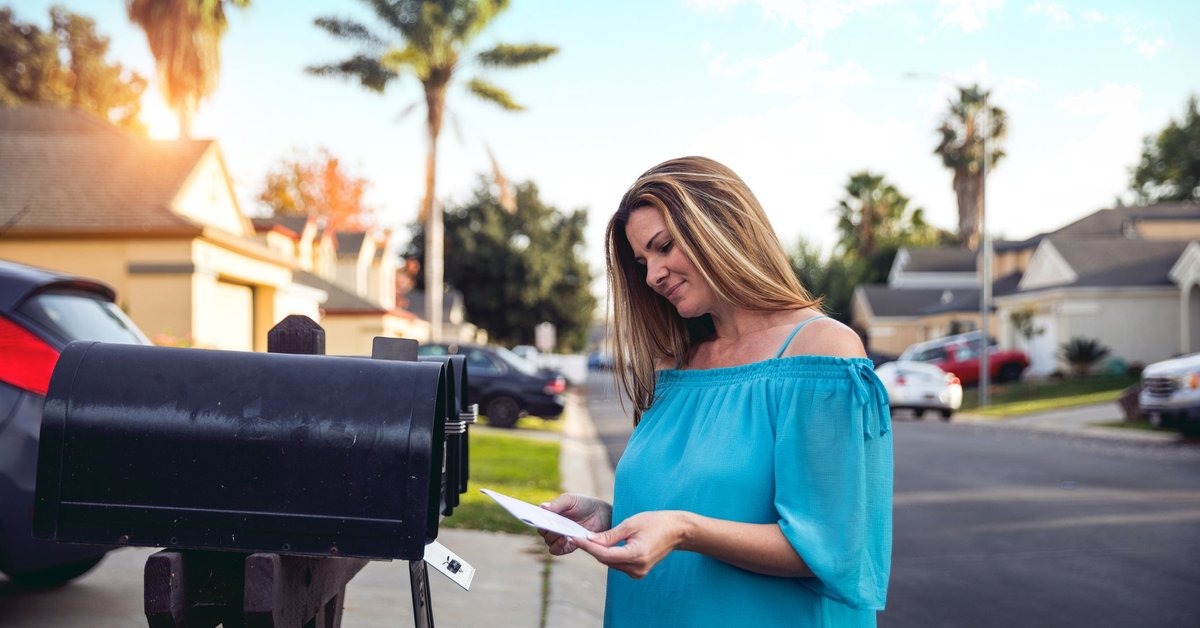 Woman checking mailbox in neighborhood with palm trees.