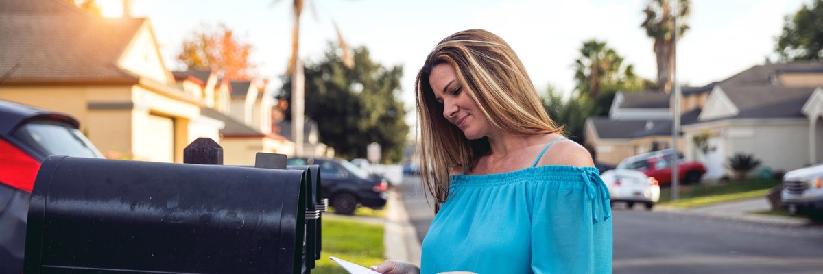 Woman checking mailbox in neighborhood with palm trees.
