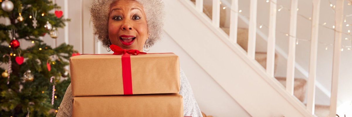 A woman standing in her decorated living room holding an armful of gifts.