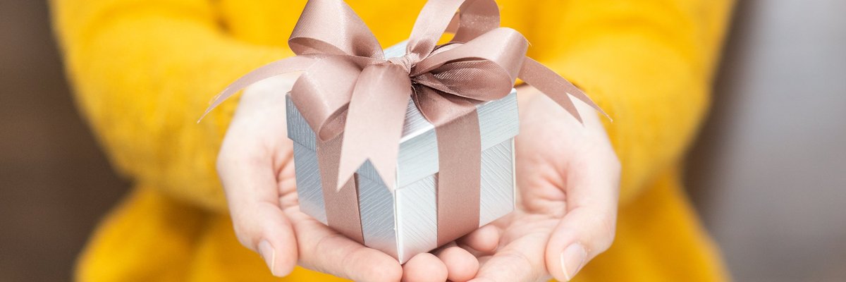 A woman in a yellow sweater holding out a wrapped gift.