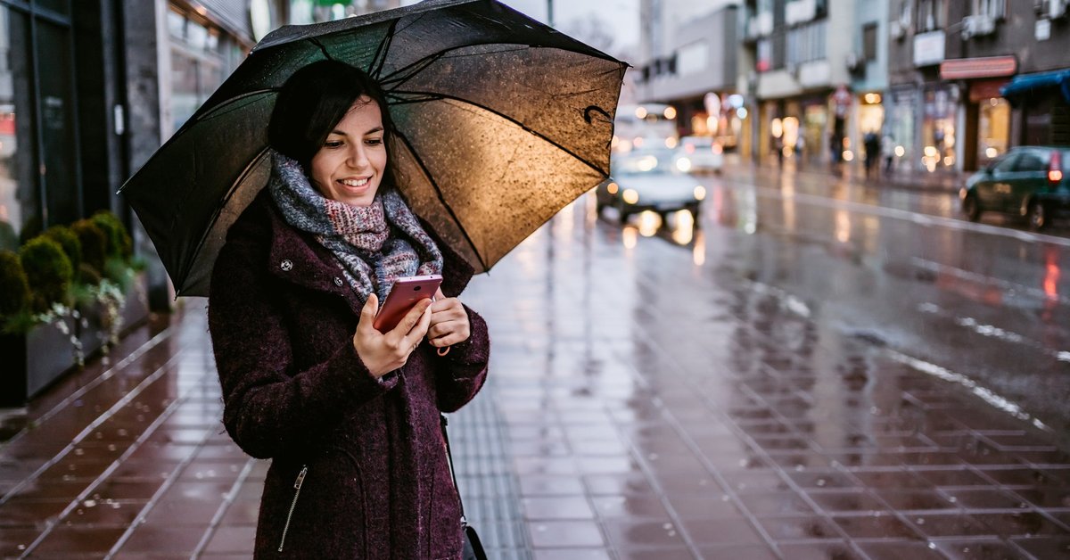 Woman holding umbrella over her head as she stands on city sidewalk in the rain
