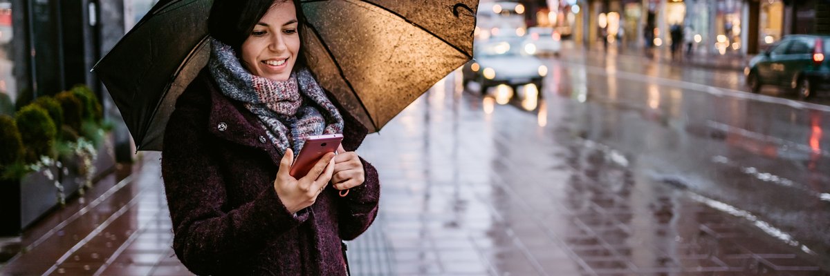 Woman holding umbrella over her head as she stands on city sidewalk in the rain