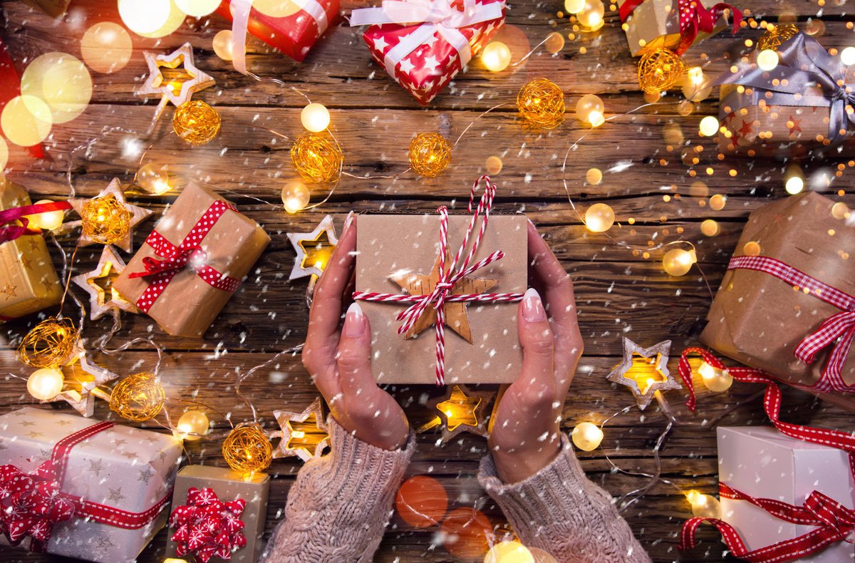 A woman's hands holding a wrapped gift over a table of lights and presents.