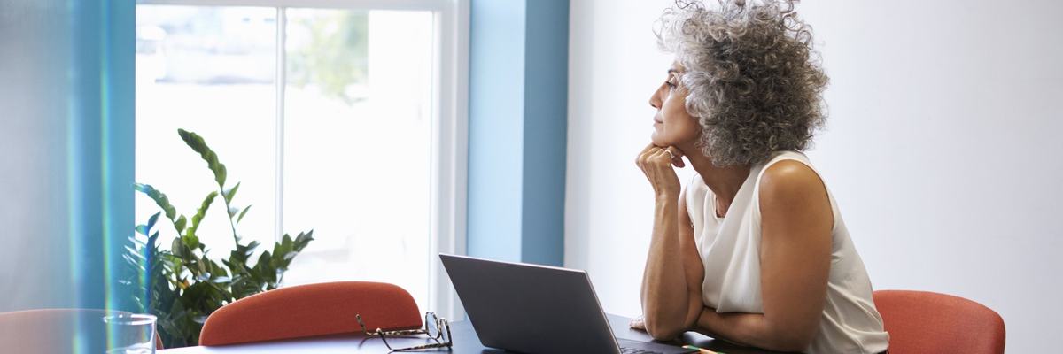 A middle-age woman sitting in an office looking thoughtful.
