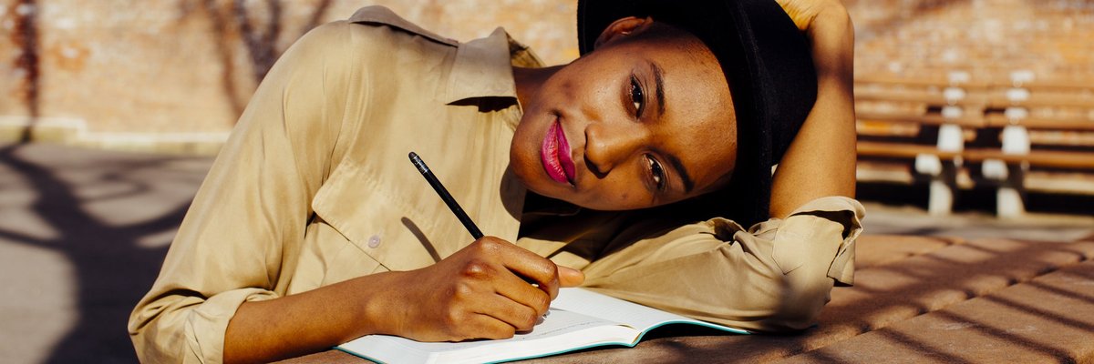 A woman sitting at a sunny park table and writing in a journal.