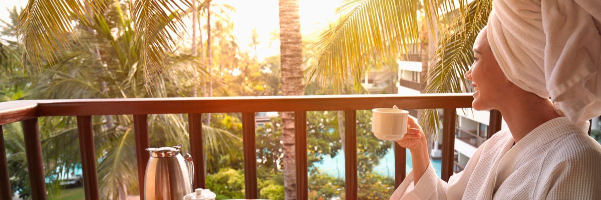 Woman in robe drinking coffee on balcony at tropical location.