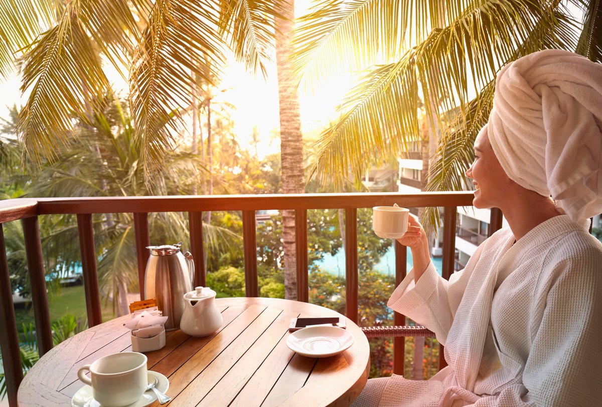 Woman in robe drinking coffee on balcony at tropical location.