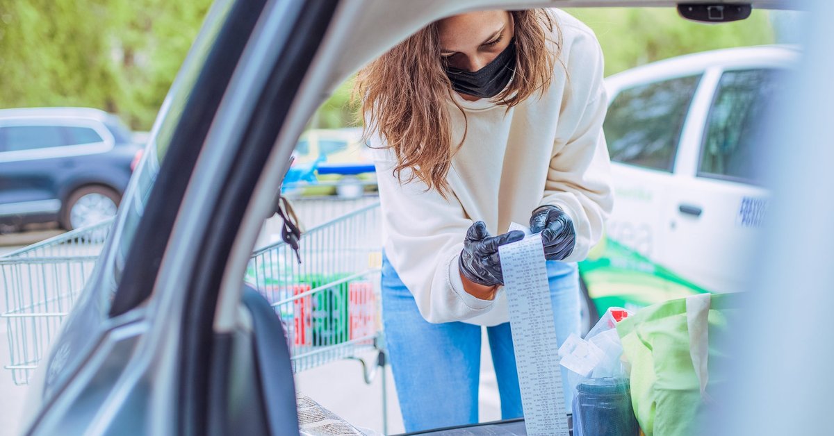 Woman loading car with groceries looks over her receipt closely.