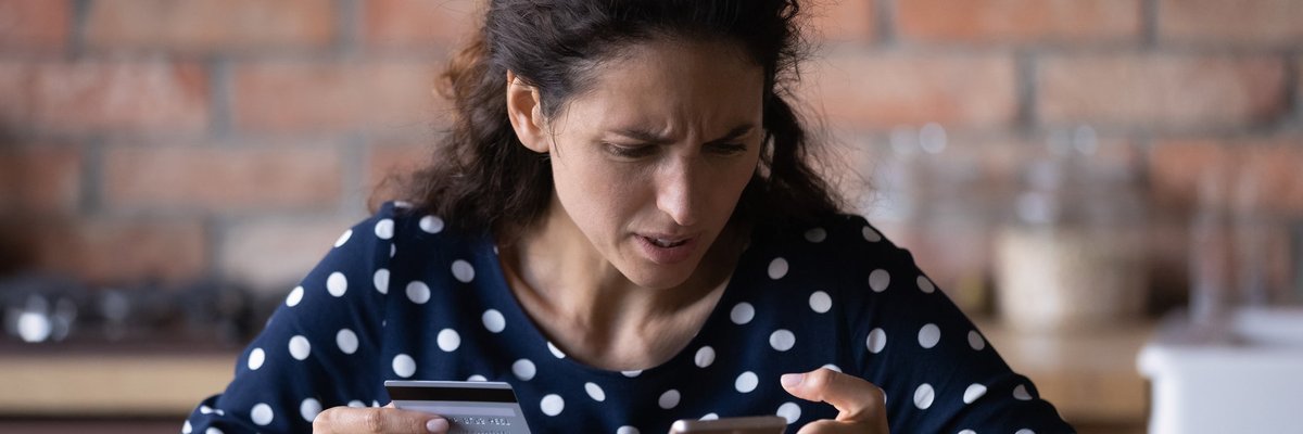 Woman looking at her cell phone in frustration as she holds a credit card in her other hand.