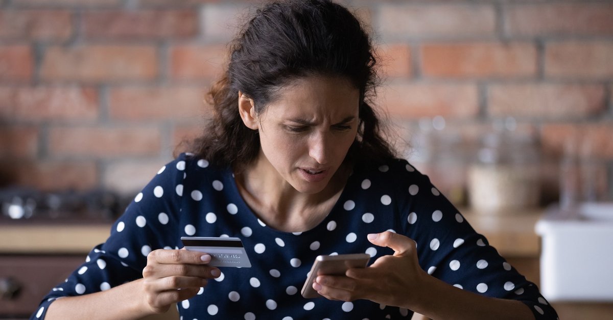 Woman looking at her cell phone in frustration as she holds a credit card in her other hand.