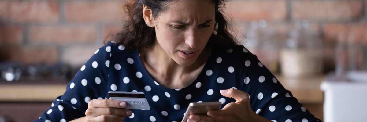 Woman looking at her cell phone in frustration as she holds a credit card in her other hand.