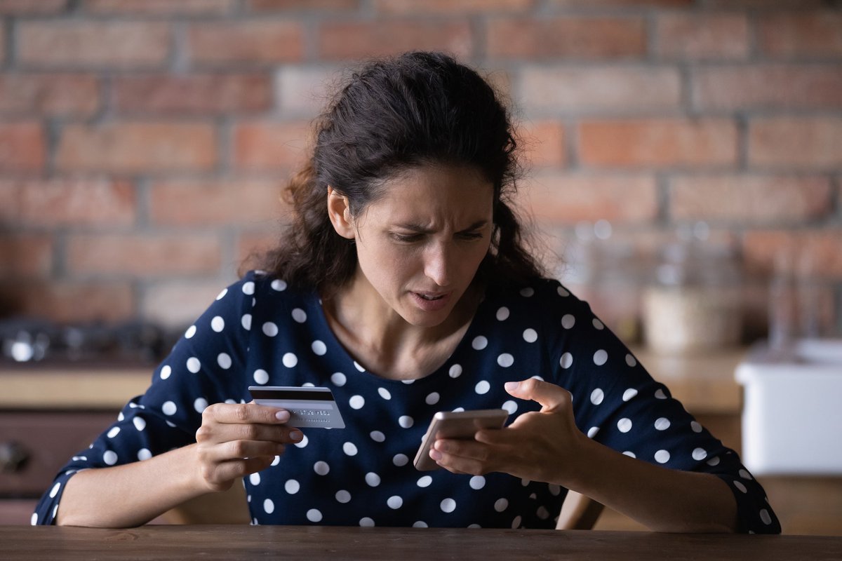 Woman looking at her cell phone in frustration as she holds a credit card in her other hand.
