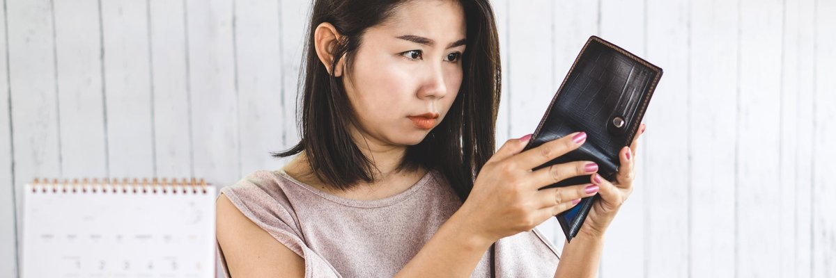 Woman looking in empty wash with credit cards, calculator, and alarm clock on desk in front of her.
