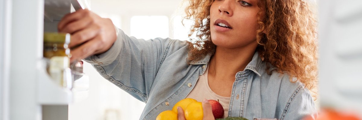 A woman putting fruits and vegetables away in her refrigerator.