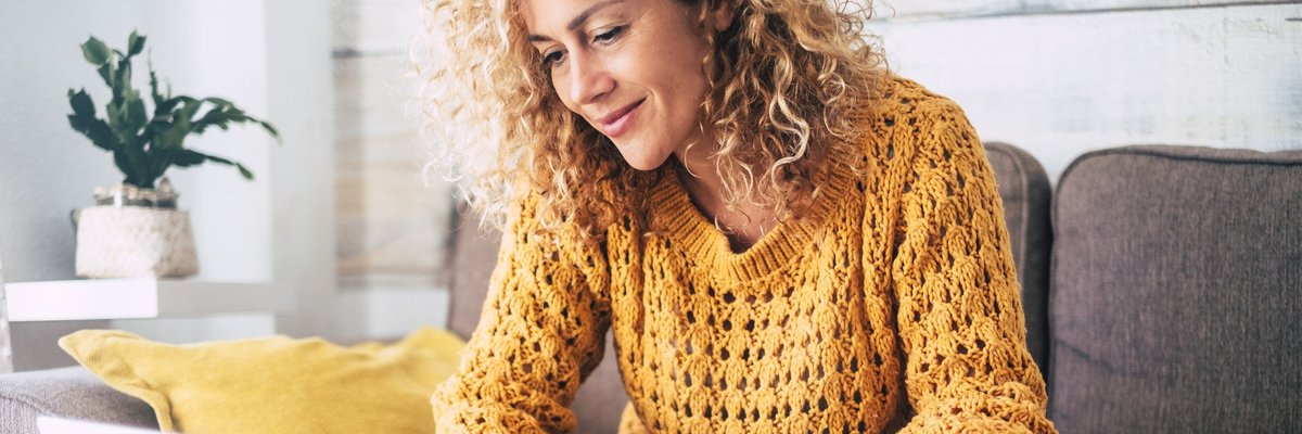 A woman sitting on her couch with a laptop and a cup of coffee.