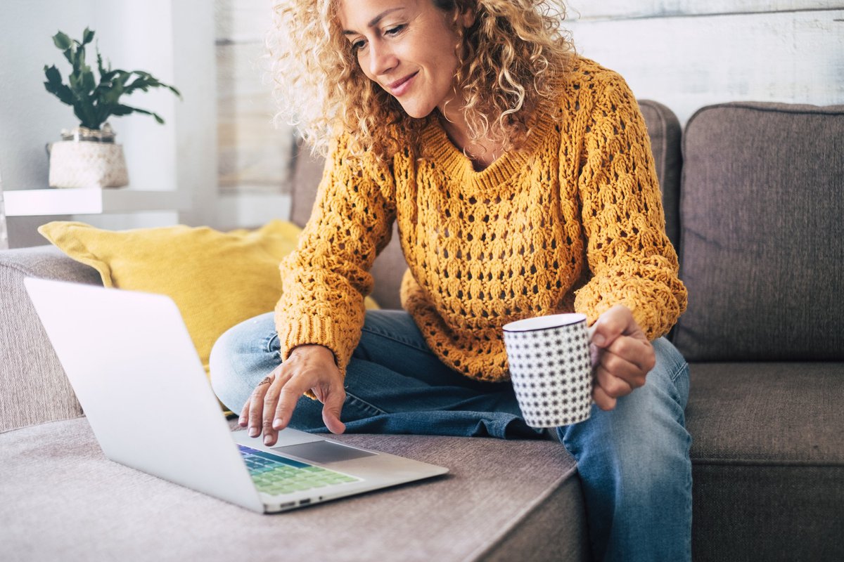 A woman sitting on her couch with a laptop and a cup of coffee.