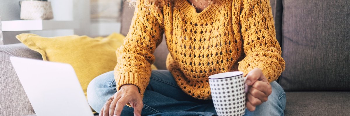 A woman sitting on her couch with a laptop and a cup of coffee.