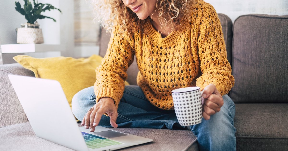 A woman sitting on her couch with a laptop and a cup of coffee.