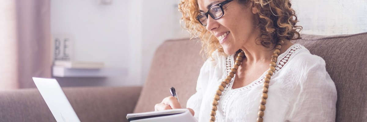 A woman sitting on a couch with a notebook and laptop.