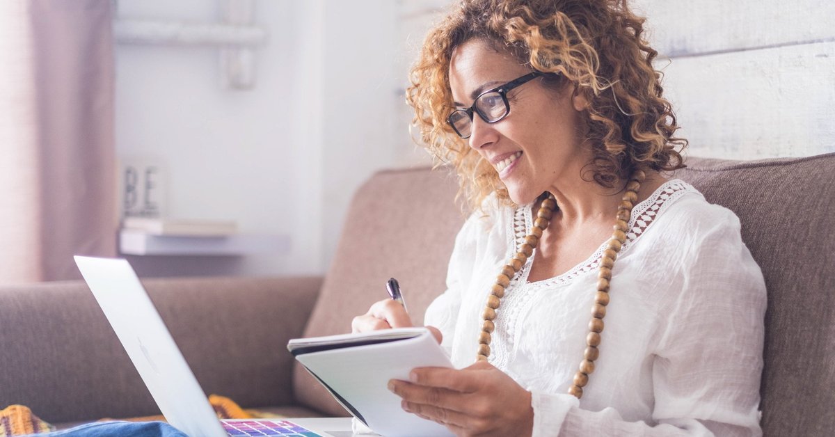 A woman sitting on a couch with a notebook and laptop.