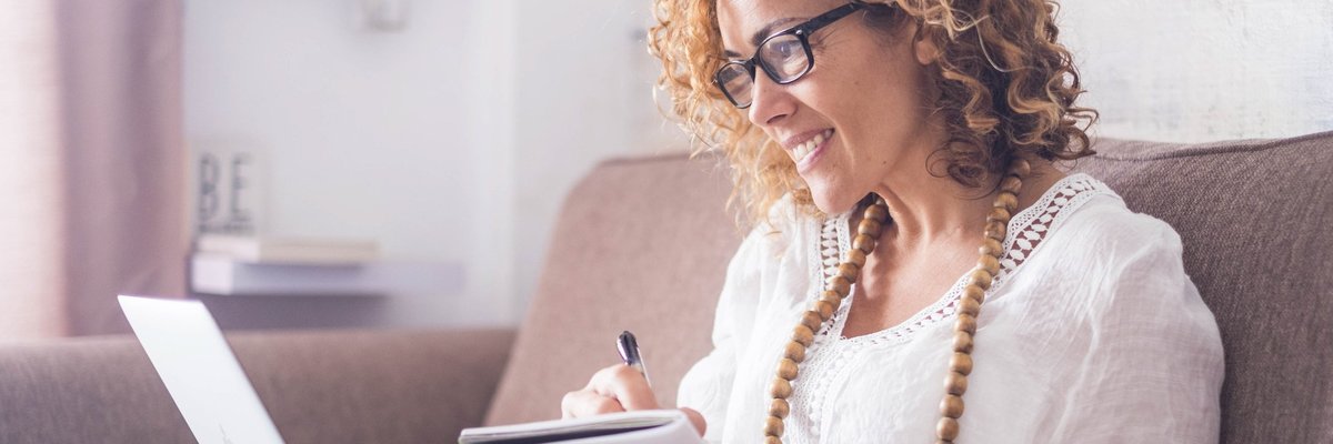A woman sitting on a couch with a notebook and laptop.