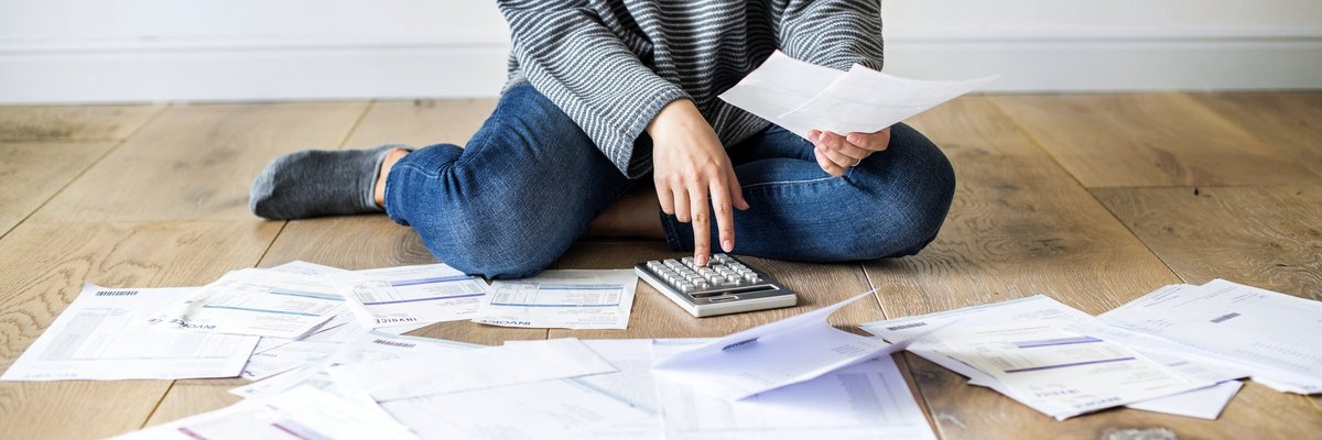 A woman sitting on floor with paper bills and a calculator.