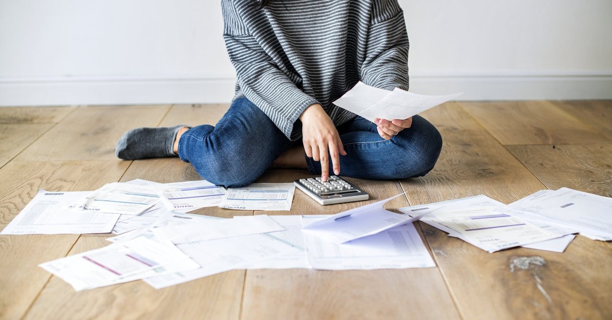 A woman sitting on floor with paper bills and a calculator.