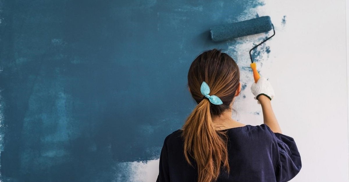 Woman painting home blue with a roller.