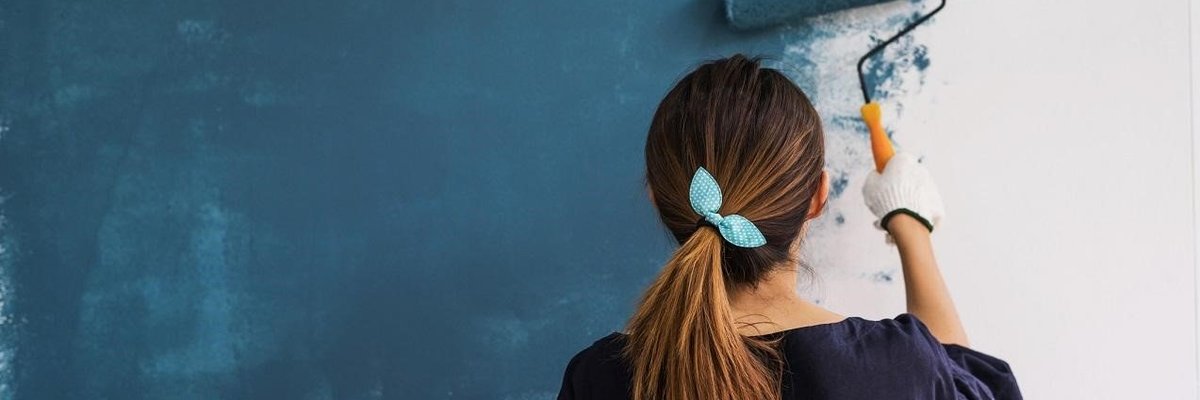 Woman painting home blue with a roller.