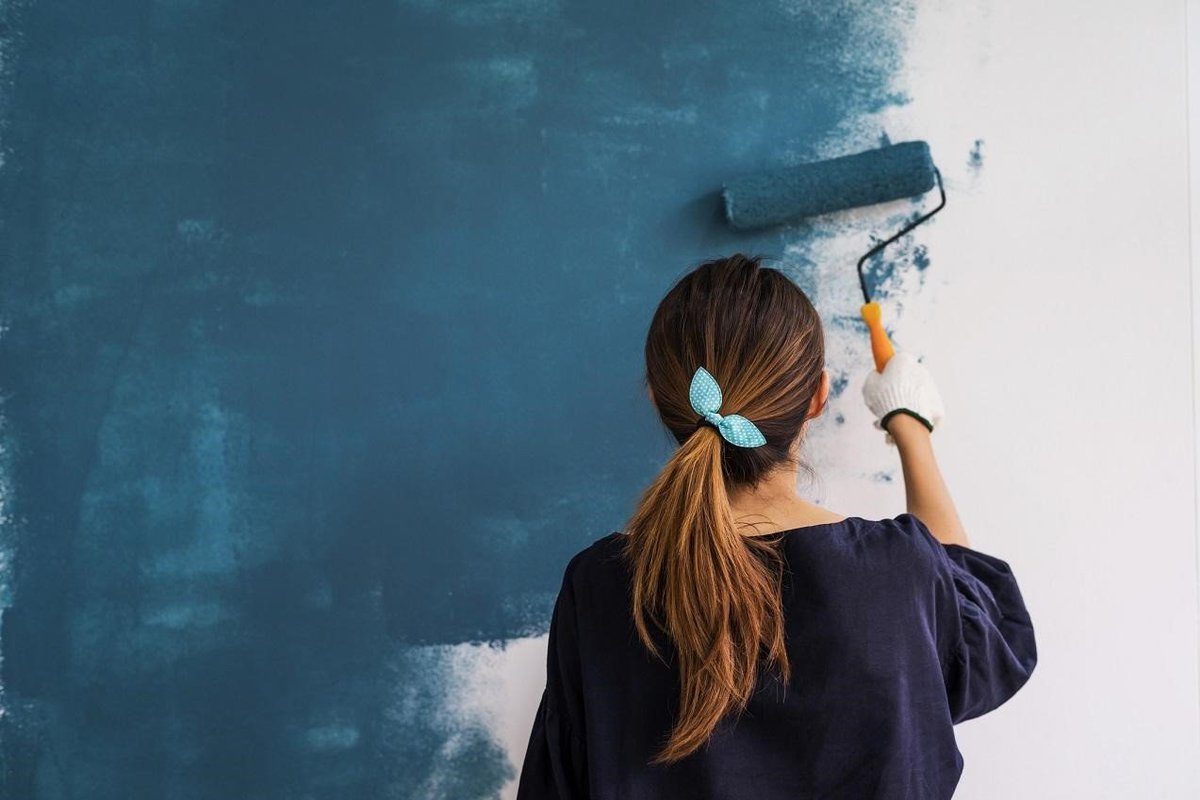 Woman painting home blue with a roller.