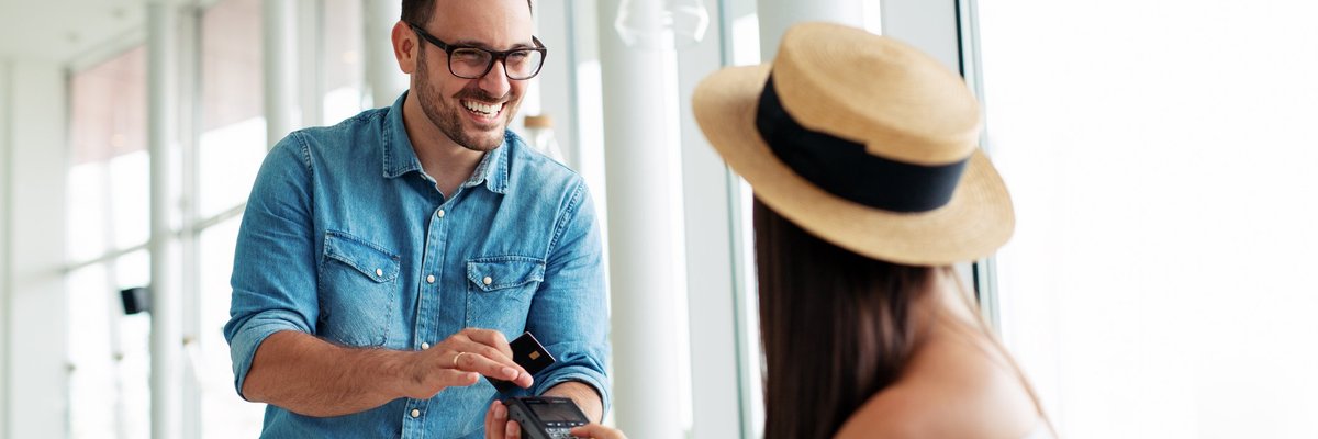 A young woman in a hat paying a waiter with her credit card.