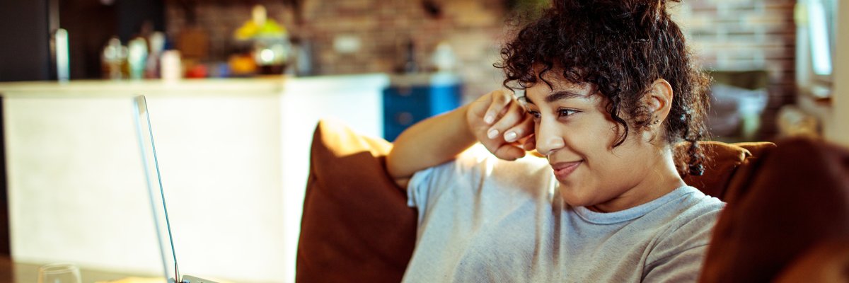 A woman sits on her sofa, looking at her laptop.