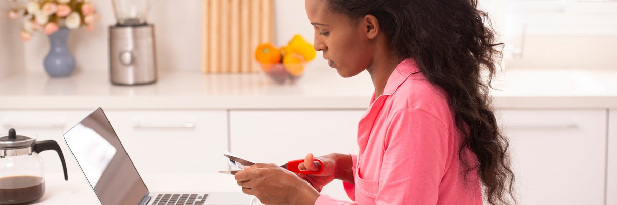 Woman sitting in front of her laptop cutting up a credit card.