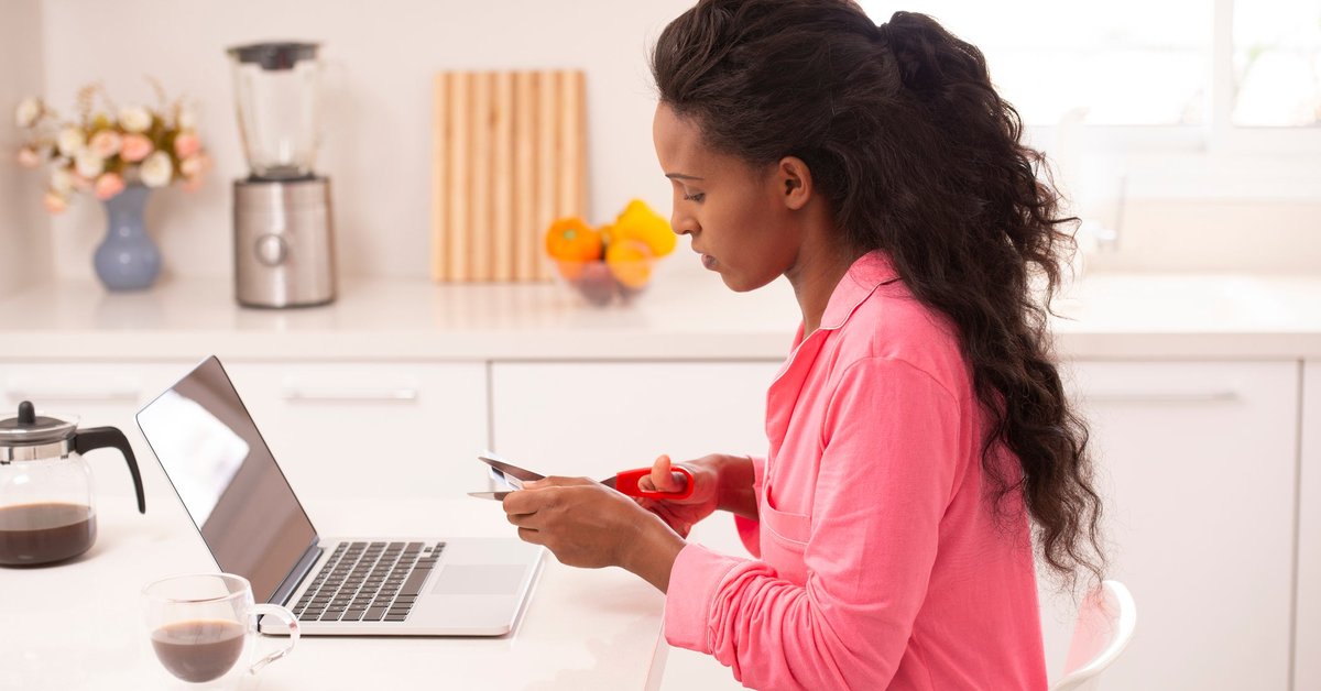 Woman sitting in front of her laptop cutting up a credit card.