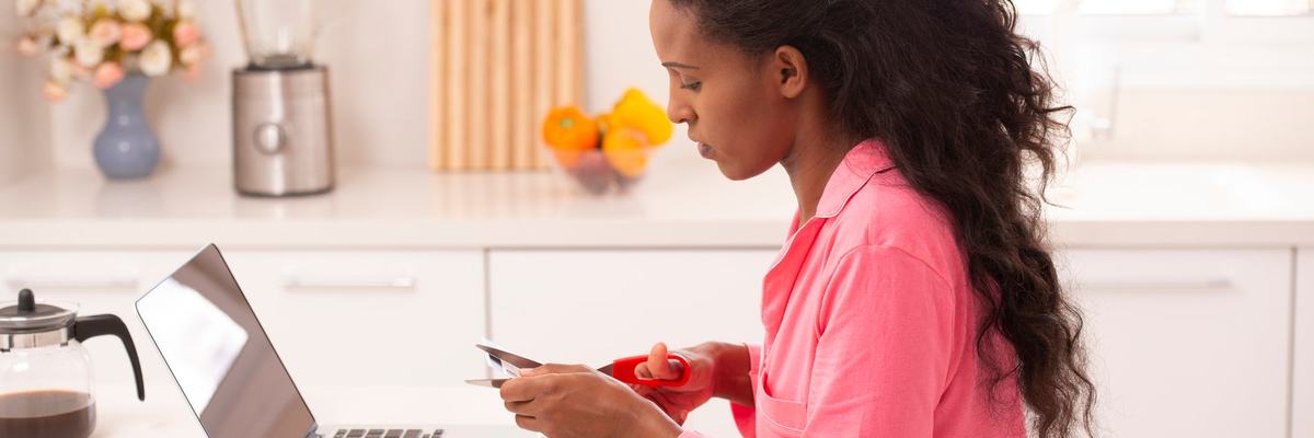 Woman sitting in front of her laptop cutting up a credit card.