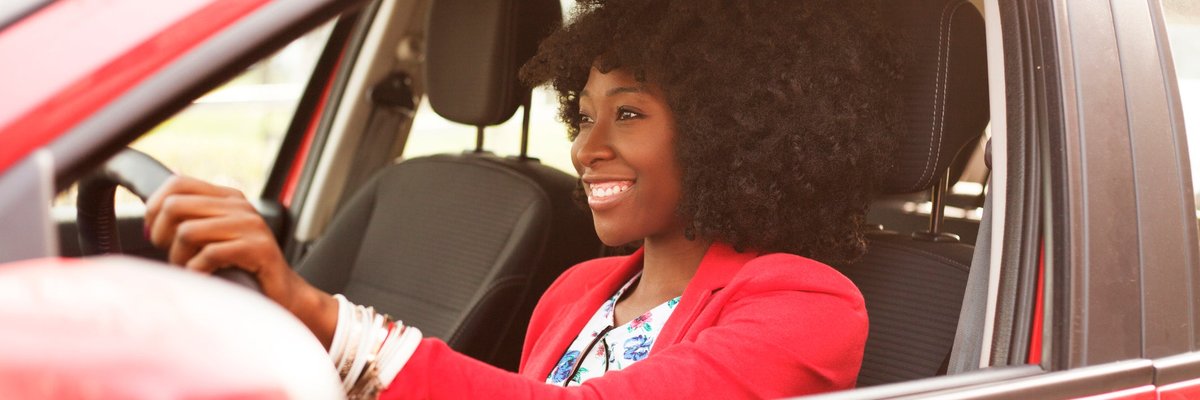 Woman smiling as she drives a red vehicle.