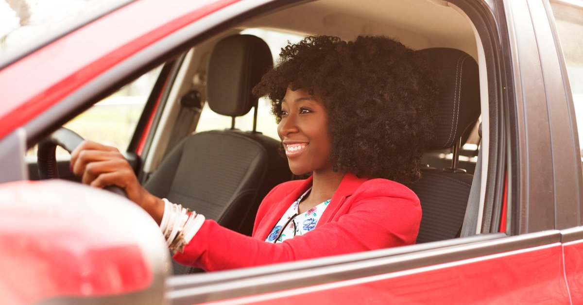 Woman smiling as she drives a red vehicle.