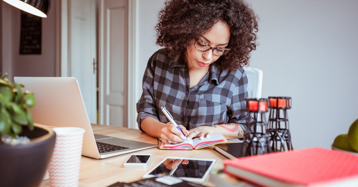 Woman taking notes while using a laptop