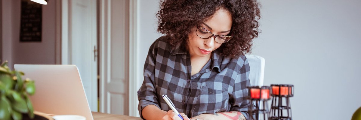 Woman taking notes while using a laptop