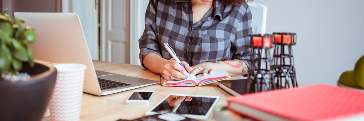 Woman taking notes while using a laptop