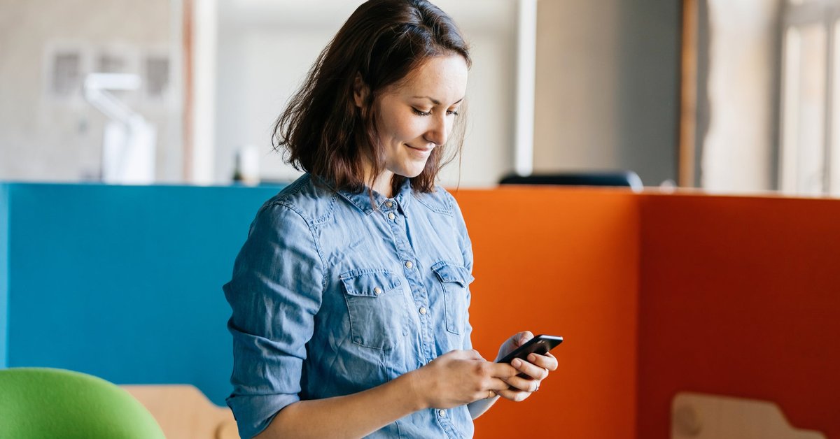 A woman stands at work, looking at her cellphone.