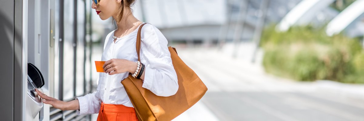 A woman using an ATM on a sunny street.