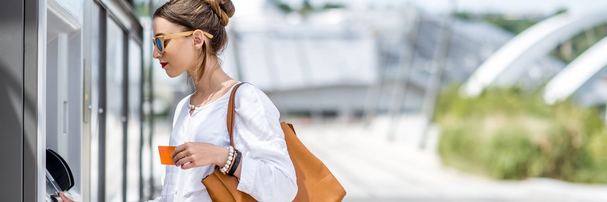 A woman using an ATM on a sunny street.