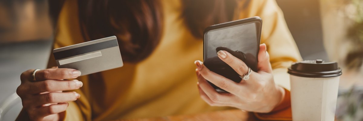 A woman at a table with a credit card, notebook, phone, and coffee cup.