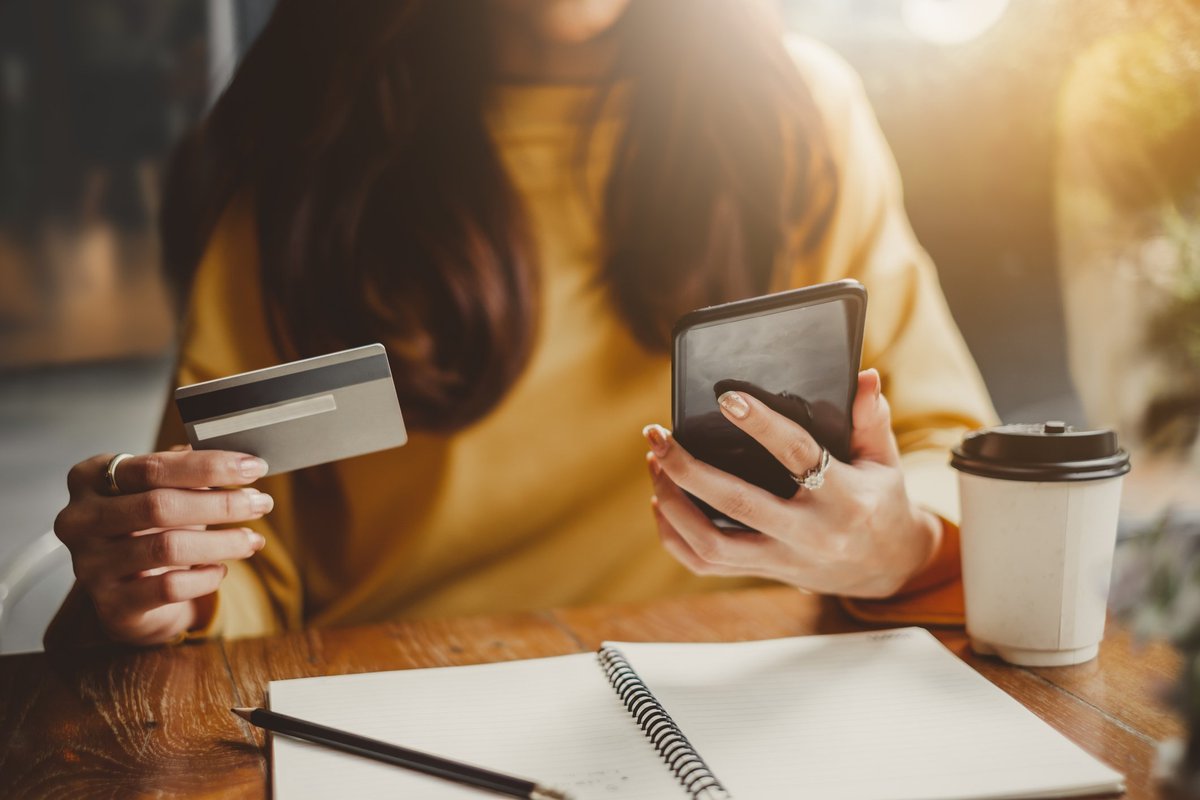 A woman at a table with a credit card, notebook, phone, and coffee cup.
