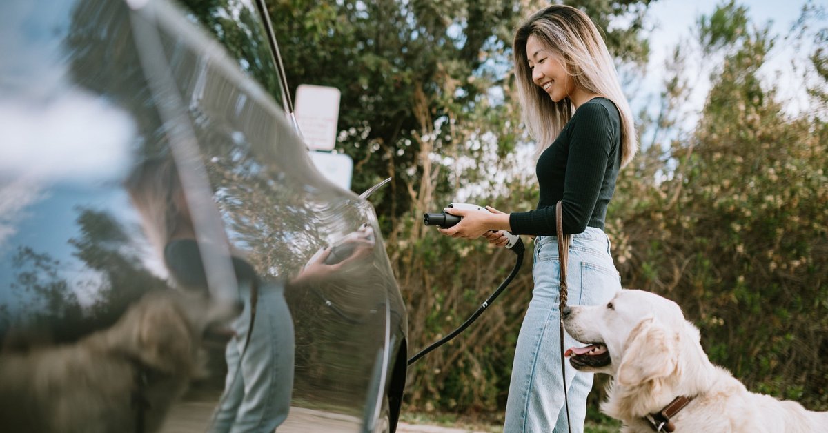 Woman with dog about to charge her electric car.